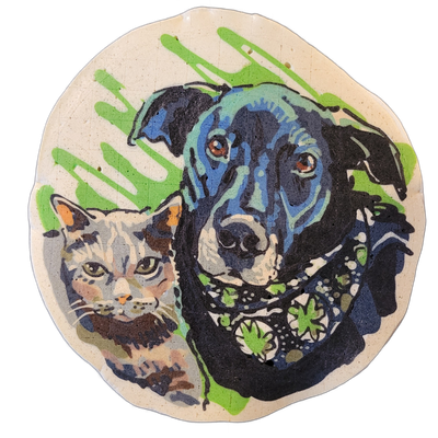 Pancake art depicting two pets side by side: a dark-coated dog with brown eyes occupying the right and upper portion of a circular piece, and a calico-patterned cat with green eyes positioned in the lower left, both shown from approximately the chest up; the dog wears a collar with a leaf pattern r…
