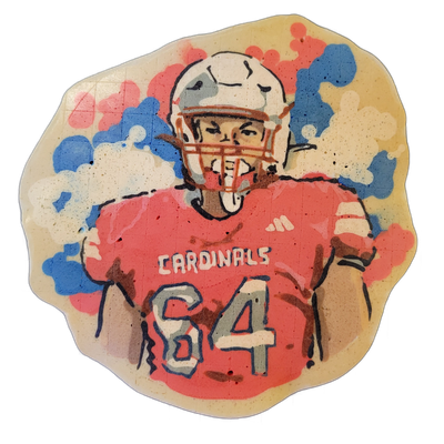 Pancake art portrait of a football player named Mason, shown from the waist up, wearing a red jersey labeled 'CARDINALS' with the number 64, a white helmet, and an orange face mask. Dan illustrated the piece with bold black outlines, red and white batter fill for the uniform, and a background of lo…