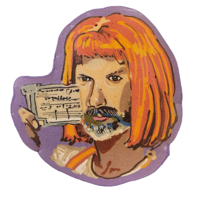 Pancake art depicting a figure with orange-red bob-length hair, a mustache and multicolored beard, holding up a small rectangular card printed with text and lines near their face; the figure wears a white garment with orange and yellow stripes at the shoulder. Rendered by Dan with bold dark outline…