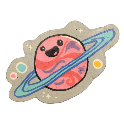Saturnina, a JoP original character depicted as a cartoon planet with a simple face — two dot eyes and a small open mouth rendered in black — encircled by a broad, layered ring system angled diagonally across the composition, surrounded by small star shapes and two smaller orbs (one teal, one yello…