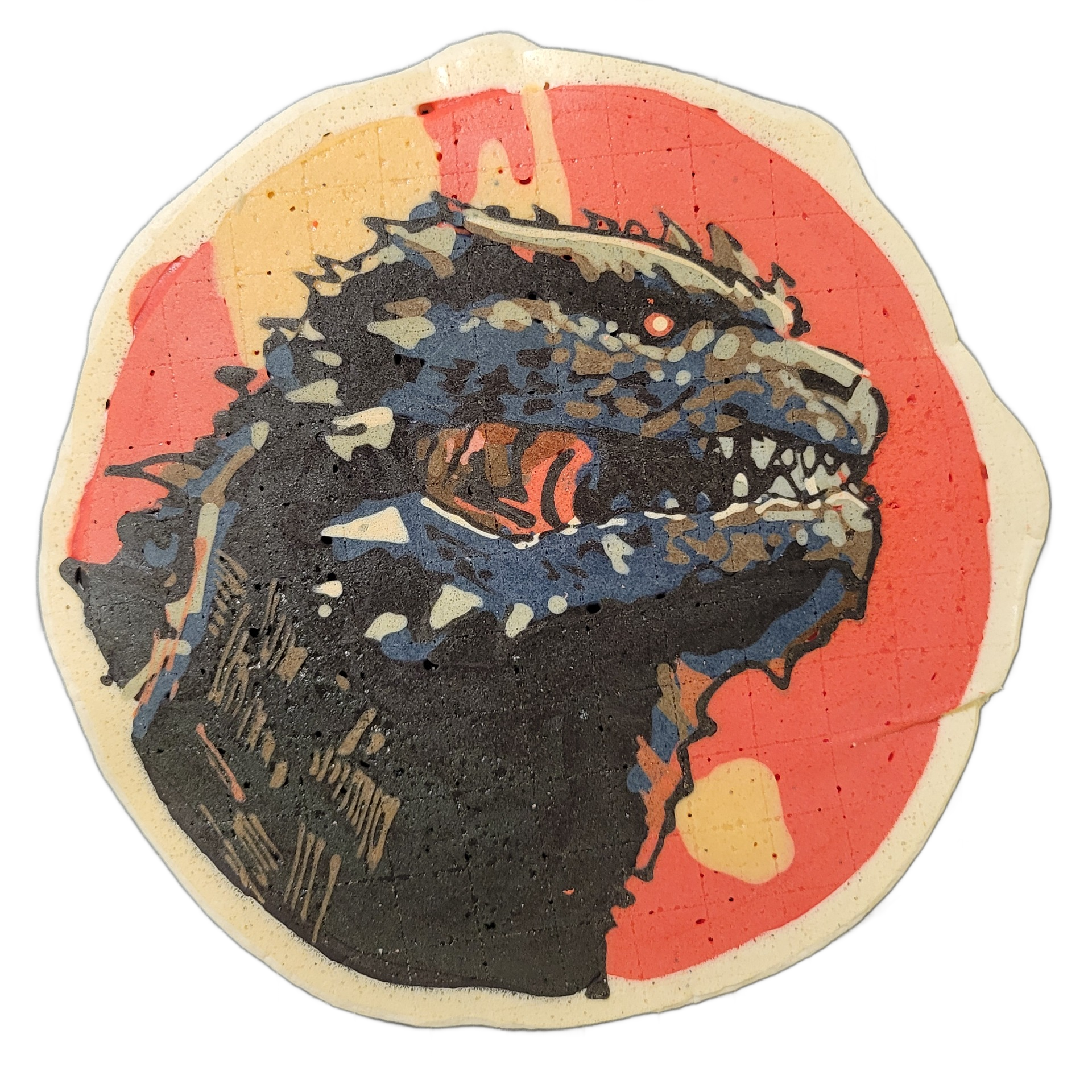 Pancake art depicting Godzilla, shown as a close-up portrait of a large reptilian creature's head and upper body in profile, mouth open wide with visible teeth and tongue, a single red eye visible, and a row of dorsal spines along the top of the head and back. The image uses bold black outlines fil…