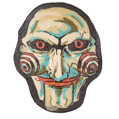 Pancake art of a face called Jig, with pale cream skin, red-irised eyes set in dark shadowed sockets, a long narrow nose, red-outlined lips with drip-like extensions below the chin, and red-and-teal spiral decorations on both cheeks. Dan rendered it with bold dark outlines, filled with teal, olive,…