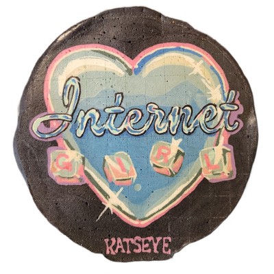 Pancake art depicting a blue heart shape containing the word 'Internet' in cursive script and four letter-block dice spelling out 'GIRL,' with the name 'KATSEYE' printed in block letters along the bottom edge. The piece uses bold black outlines, a palette of sky blue, pink, violet, and white with s…