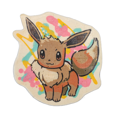 Pancake art of a small brown fox-like creature named Evie, shown seated and facing forward with large pointed ears, wide round eyes, a cream-colored ruff at the chest, and a bushy tail with layered brown and cream coloring. Rendered with bold black outlines over warm brown, orange, and cream batter…