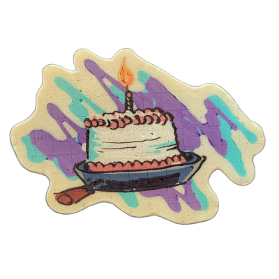 Pancake art depicting a slice of layered cake on a plate with a single lit candle on top, accompanied by what appears to be a small handle or utensil extending from the lower left of the plate. The piece uses bold dark outlines with fill areas in white, salmon pink, and slate blue for the cake and…