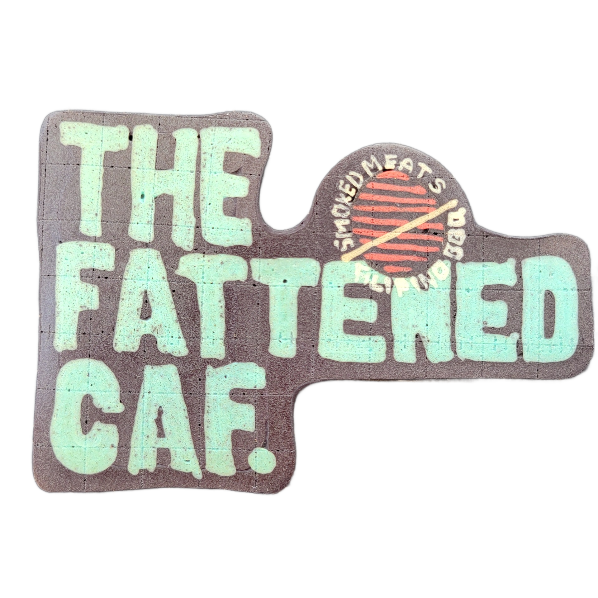 Pancake art depicting the text 'THE FATTENED CAF.' in large, bold teal block letters on a dark brown background, with a circular logo element in the upper right showing a stylized round grill grate in red and brown with two crossed drumsticks or skewers, surrounded by the curved text 'SMOKED MEATS'…