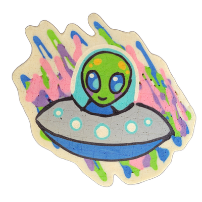 Pancake art depicting Trav, a green alien character with large blue eyes, small yellow spots on the head, and a slight smile, shown from the chest up inside a gray flying saucer with teal and white circular details and a blue rim band. The piece uses bold black outlines with flat color fills in gre…