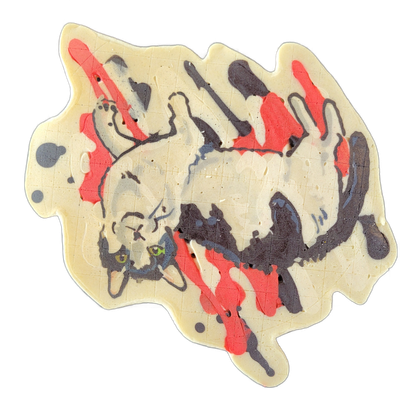 Pancake art of a cat named Juliette, depicted lying on its back in a relaxed pose with its head turned toward the viewer and green eyes visible. The piece uses fine dark outlines to define the cat's form against a cream-colored background, with bold drip-style streaks of red and dark purple-gray ba…