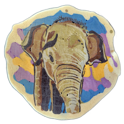 A front-facing elephant head rendered in pancake art, centered on a roughly circular piece with an irregular scalloped edge, set against a background of overlapping blue, violet, and yellow batter areas. The elephant is illustrated with bold dark outlines and layered brown and tan tones, with visib…