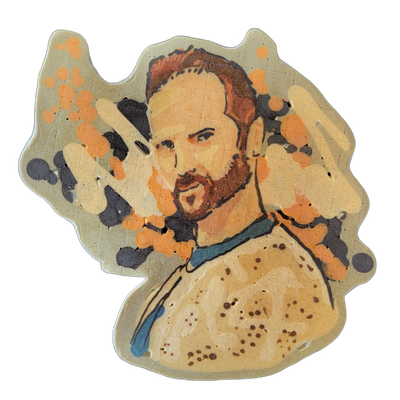 Pancake art portrait of a bearded man named Otto, shown from the chest up, facing slightly left, with short reddish-brown hair and a beard, wearing a light-colored shirt with a teal collar or scarf detail, surrounded by abstract splatter shapes in orange and dark gray-black radiating outward from h…