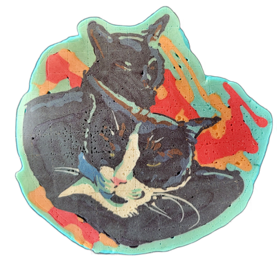 Pancake art depicting two cats curled together, one larger dark cat positioned behind a smaller tuxedo-patterned cat with a white muzzle, pink nose, and visible whiskers, both with eyes partially closed. The piece uses bold dark batter for the cat forms with fine white batter lines for whiskers and…