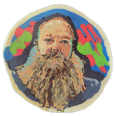 A pancake art portrait labeled 'rj' depicting a person with a large, long, wavy beard rendered in layered browns, tans, and white streaks, with dark shoulder-length hair framing a round face with visible eyes, nose, and mustache area; the head is set against a dark navy-to-black background decorate…