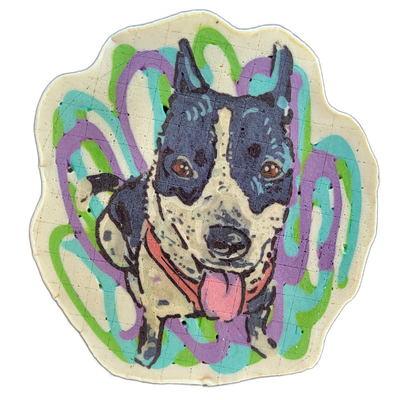 A pancake art portrait of a dog with pointed ears, a black-and-gray mottled coat, a white muzzle and chest with dark speckles, brown eyes, a pink tongue extended, and a red collar, centered on a scalloped-edge cream-colored base.