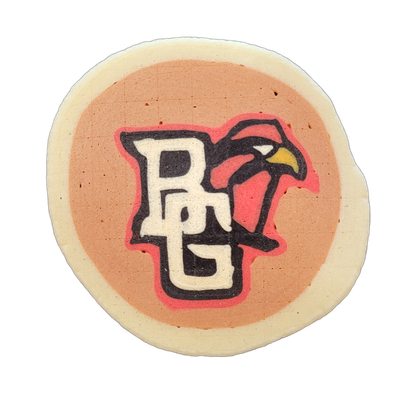 Pancake art depicting the letters 'BG' in white block lettering with black outlines and a red shadow layer, overlaid with a bird head in profile facing right — the bird has a red and dark body, a yellow beak, and a white eye marking, rendered against a tan circular field with a white irregular bord…