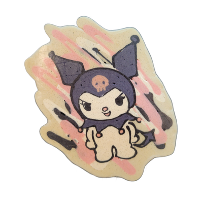 A pancake art piece depicting a small cartoon character with large dark purple rabbit-like ears, a round dark purple head bearing a small skull emblem on the forehead, a white face with angular eyes and an open mouth, and a body dressed in a dark purple costume with a ruffled collar dotted with sma…