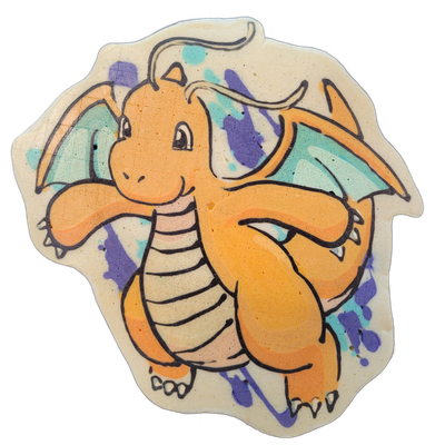 Pancake art depicting Dragonite, a large orange dragon-like character with small wings, a rounded body, a curled antenna on its head, a cream-colored segmented belly, and stubby clawed limbs posed facing forward with arms slightly raised. Bold black outlines define the figure, with orange and pale…