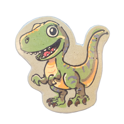Pancake art of a cartoon theropod dinosaur, depicted upright in a three-quarter facing pose with a large open mouth showing teeth, one small forearm raised, and a long tail extending behind it; the figure sits on a light beige background shaped to follow the dinosaur's silhouette. Bold black outlin…