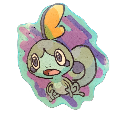 Pancake art depicting Sobble, a small teal-green lizard-like cartoon character with large round eyes, a wide open mouth showing a pink tongue, small clawed hands held in front of its body, and a curled tail; a round orange-and-green orb-shaped feature sits atop its head on a thin curved stalk. Bold…