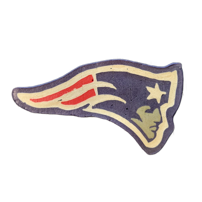 A pancake art rendering of the New England Patriots NFL logo, depicting a stylized patriot head in profile facing right, with a tricorn hat composed of red and white horizontal stripes and three sweeping white lines suggesting motion, a star shape above the face, and a simplified facial silhouette…