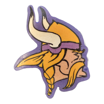 Pancake art depicting the Minnesota Vikings NFL team logo: a side-profile face of a horned Viking warrior with a braided beard, long flowing hair, a purple headband, and a horned helmet with a white curved horn, all set against a purple silhouette border. The piece uses bold dark outlines with fill…