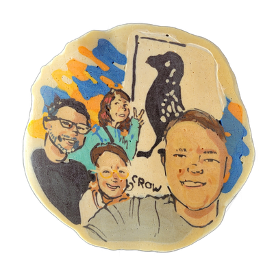 A pancake art piece depicting four people arranged in a group portrait, with a dark silhouette of a spotted bird perched on a vertical line in the upper right, and abstract splashes of blue, orange, and yellow batter filling the upper left background; the word 'SROW' appears in block lettering near…
