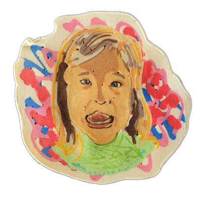 Pancake art portrait of a child named Marlow, shown from the shoulders up, with straight hair that is partly golden-yellow and partly dark brown, an open mouth showing teeth, and a green top. The portrait is rendered with fine dark outlines on a warm tan face, surrounded by large irregular splotche…