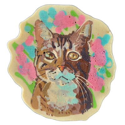 A tabby cat's face and upper chest are centered in a pancake art piece with a scalloped oval border, surrounded by clusters of pink and teal flower shapes against a green stem-like background; the cat has golden-yellow eyes, dark brown and tan striped markings, white whiskers, a small orange nose w…