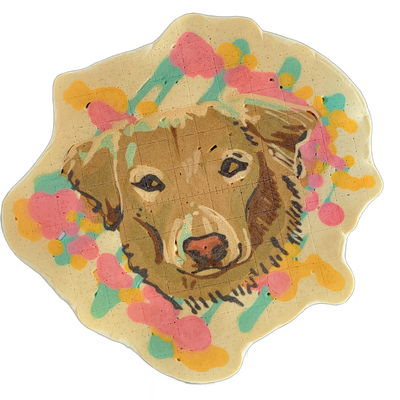 Pancake art portrait of Trout, a dog with brown and tan fur, dark eyes, a pink nose, and fur markings along the muzzle and forehead, centered on a cream-colored scallop-edged background decorated with abstract splotches and brushstroke shapes in pink, teal, and yellow. The portrait uses fine dark b…