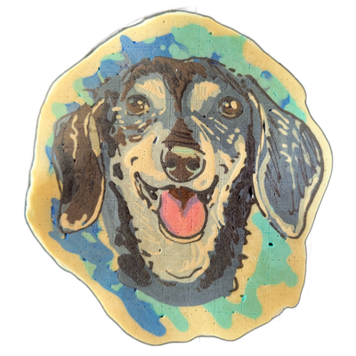 Pancake art portrait of a dog named Dunkel, shown from the shoulders up, facing forward with mouth open and tongue extended downward; the dog has long, drooping ears, a broad forehead, and a light-colored muzzle contrasting with darker fur across the head and ears. Rendered by Dan with bold dark ou…
