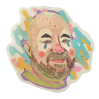Pancake art portrait of Rodeo Clown Matt, depicting a bald man with a full beard, dark arched eyebrows, and light-colored eyes, rendered with pink cheek circles, blue teardrop marks beneath each eye, and a red nose circle in a clown-makeup style. The piece uses fine batter lines for facial detail a…