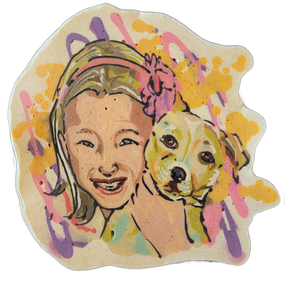 Pancake art depicting a smiling person with shoulder-length hair holding a small golden-colored dog close to their face, both facing forward; a flower or bow shape appears in the upper right area behind them. Rendered with bold black outlines and filled with peach, golden-yellow, olive, and brown t…