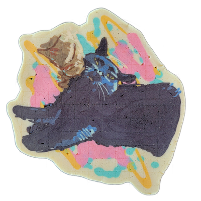 Pancake art of a dark-coated cat named Marceline, shown in a relaxed, sprawled pose with legs extended and head turned to face forward, wearing or positioned near a small hat shape at the top of the head; a second smaller animal figure, rendered in brown and cream tones, appears in the upper left.…
