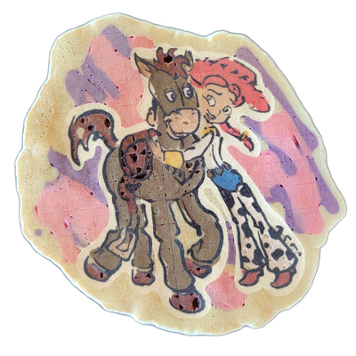 Pancake art depicting two cartoon characters named Bullseye and Jesse: a brown horse and a red-haired female figure wearing a cowboy hat, white and black spotted pants, and a yellow-accented outfit, shown together in a close pose against a background of loose pink and violet brushstroke-style fills…