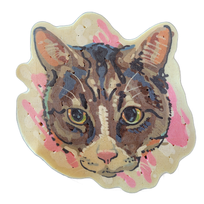 A pancake art portrait of a tabby cat face named Cat Benatar, facing forward with yellow-green eyes, a pink nose, orange inner ears, brown and dark gray striped markings, and white whiskers and muzzle fur against a cream-colored background with pink paint-splash-style batter accents on the sides. D…