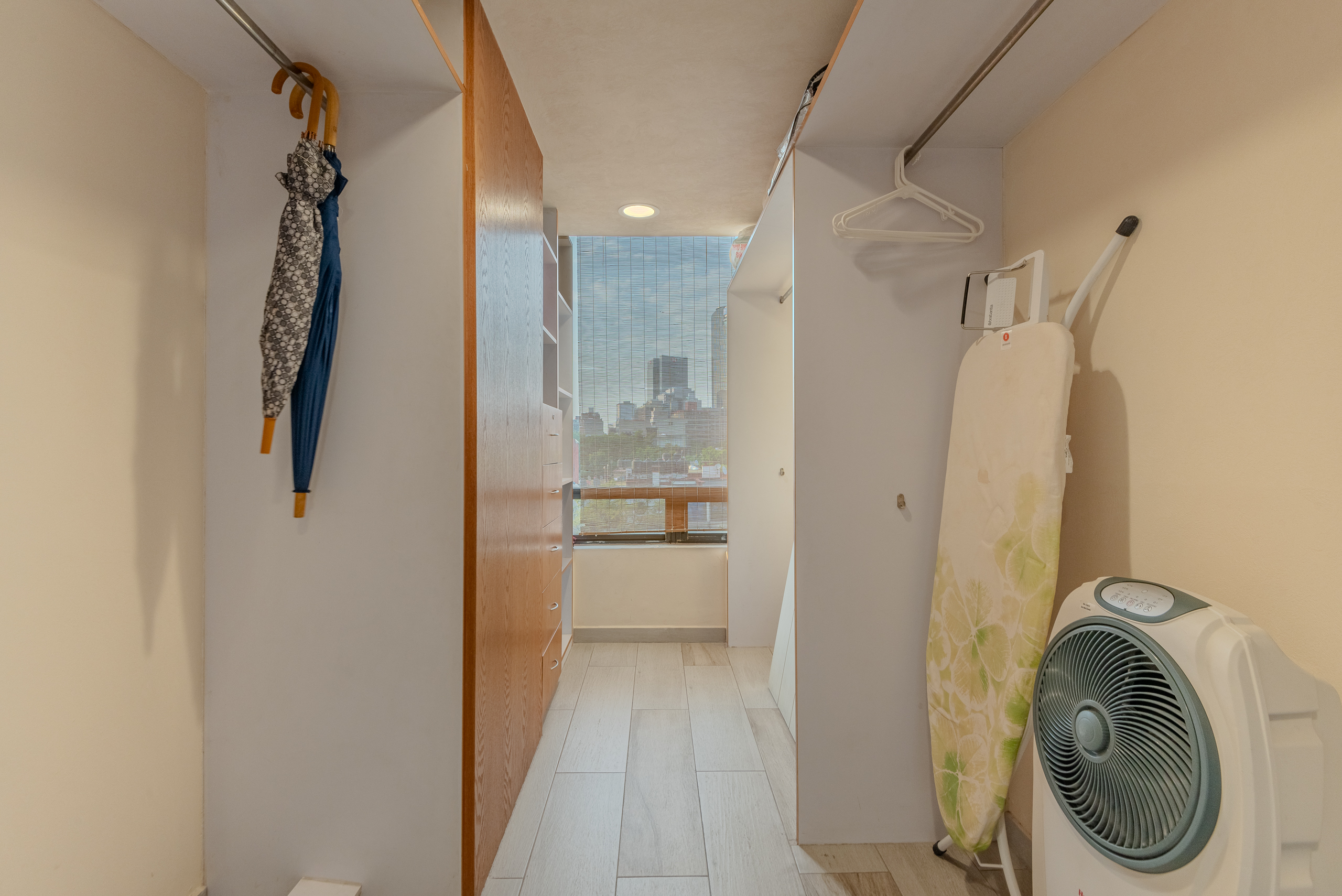 Hallway closet with an ironing board and floor fan.