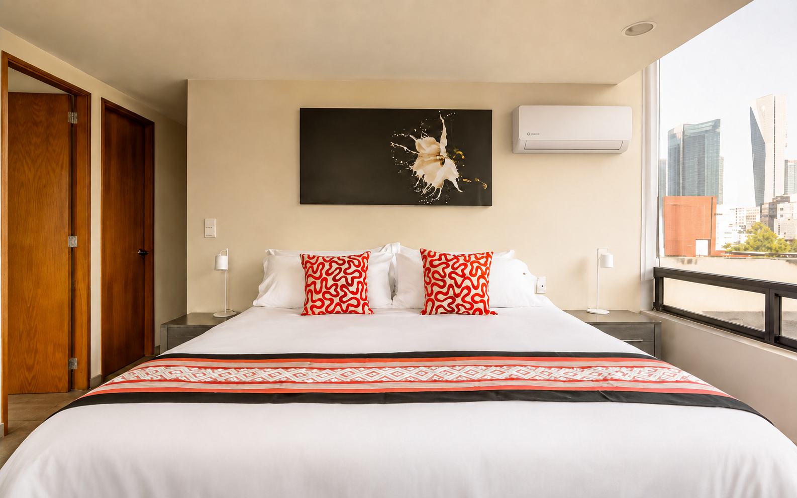 King bed beneath wall art, with a wall-mounted air conditioner and city-facing window.