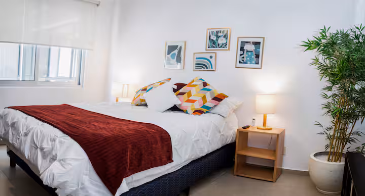 Bedroom with a bed, wall art, bedside table, and potted plant.
