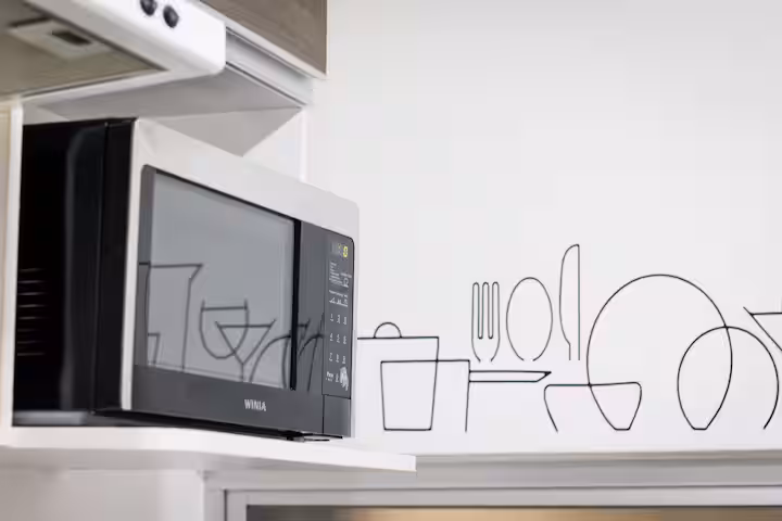 Microwave on a kitchen shelf beside line art.