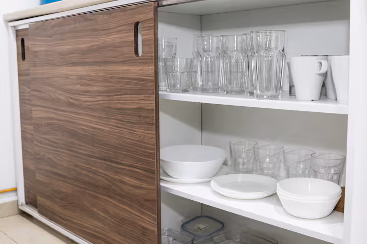 Open kitchen cupboard with glasses, bowls, and plates.