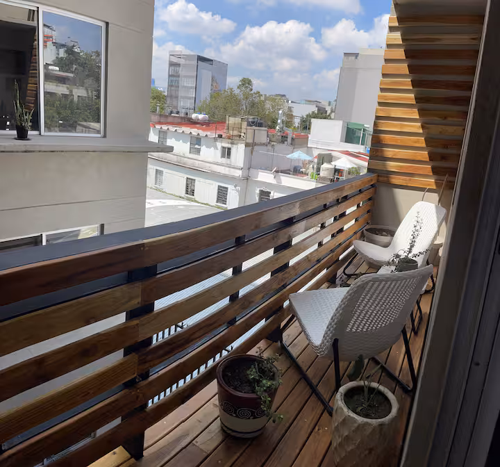 Balcony with a small table, chairs, planters, and city buildings beyond.