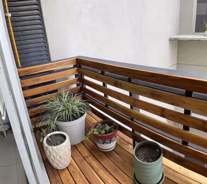 Narrow balcony with a wood railing and potted plants.