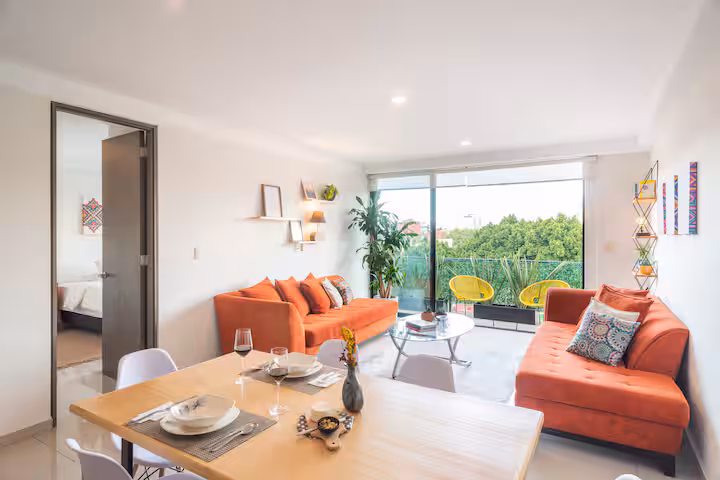 Dining table beside rust-colored sofas and wide windows.