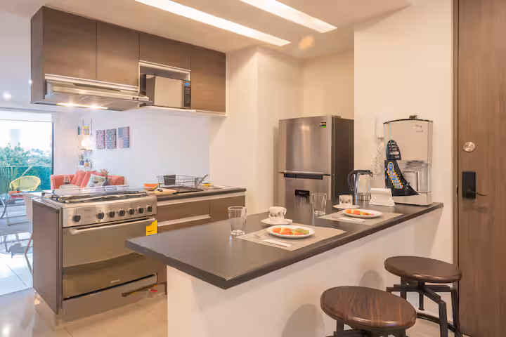 Kitchen with an island, stools, stove, refrigerator, and coffee maker.