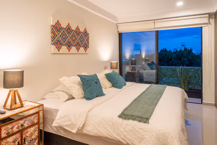 Bedroom with a bed, bedside lamps, and a city-facing window.