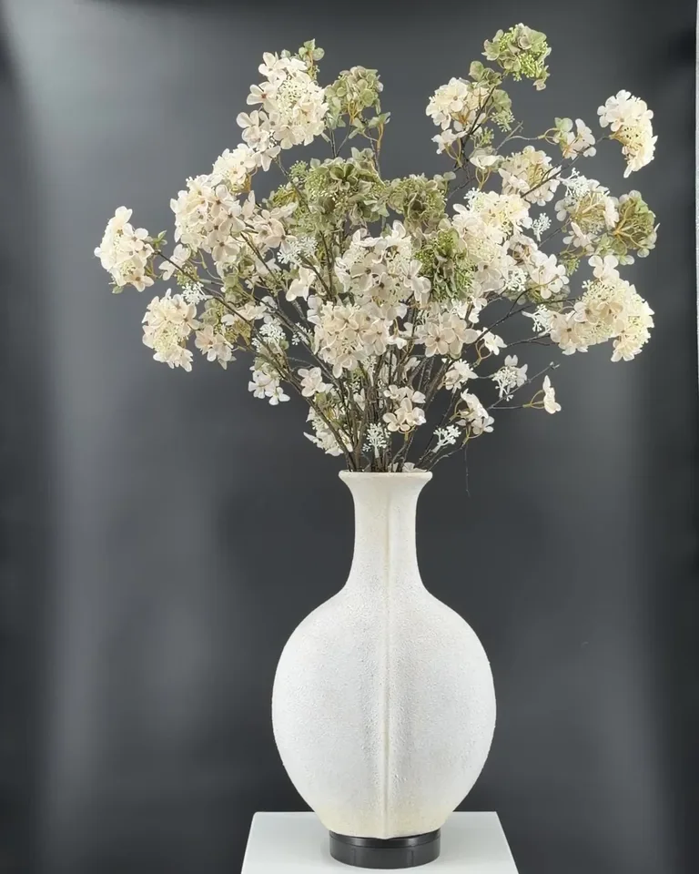 Alvara veldboeket met crème-witte en groene hortensia’s in witte vaas op sokkel