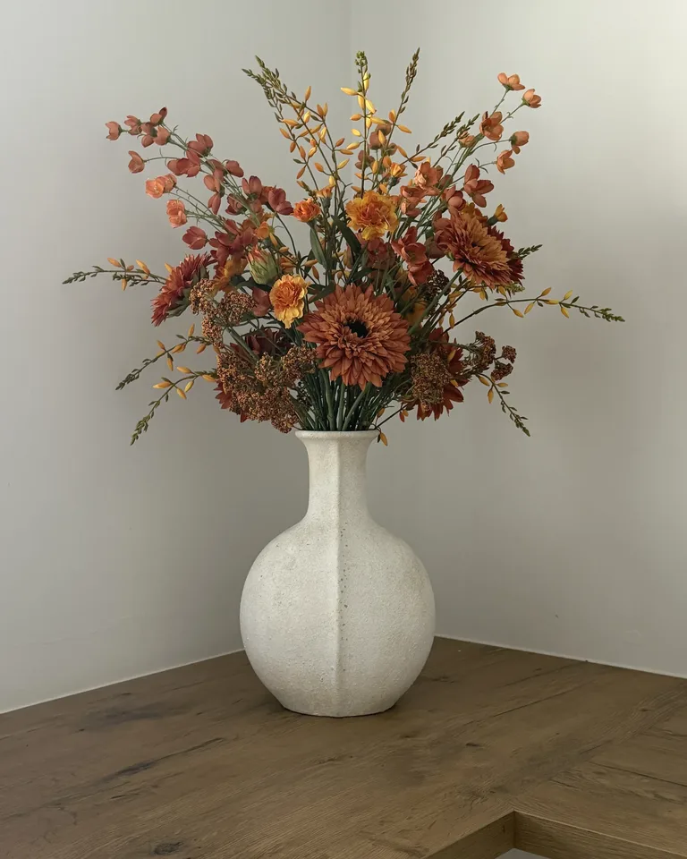 Oranje-roestkleurig boeket met dahlia’s in een witte vaas op een houten keukenblad.