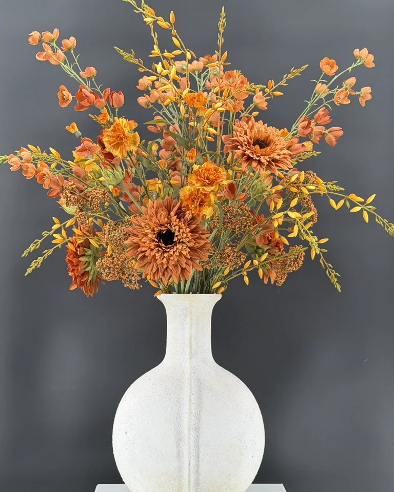 Oranje-roestkleurig boeket met dahlia’s en fijne takken in een witte vaas op een sokkel.