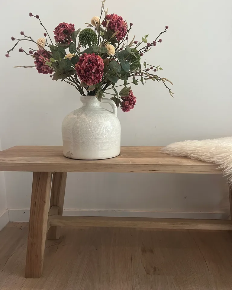 Mirelle met oudroze bloemen en groen blad in een alternatieve lichte vaas op een houten bankje.