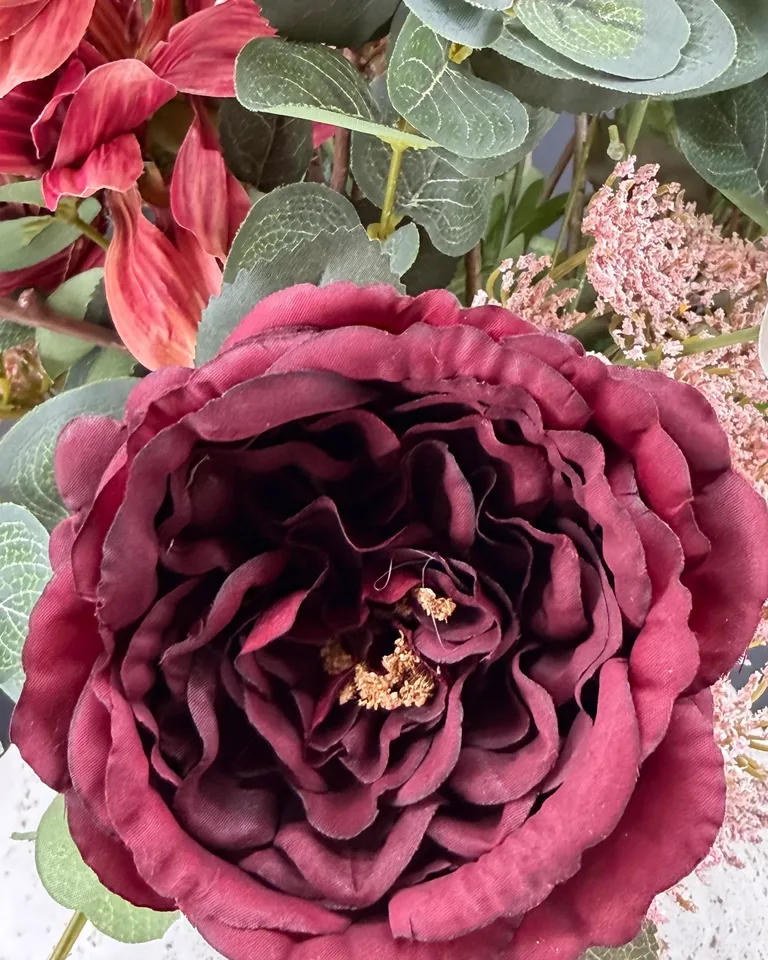 Detail van een donkerbordeaux bloem met grijsgroen blad en fijne roze takjes in Arielle