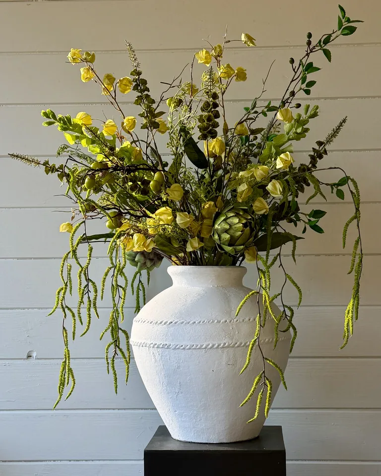 Groot groen veldboeket Verdea in een witte vaas op een zwarte pedestal in een licht interieur.